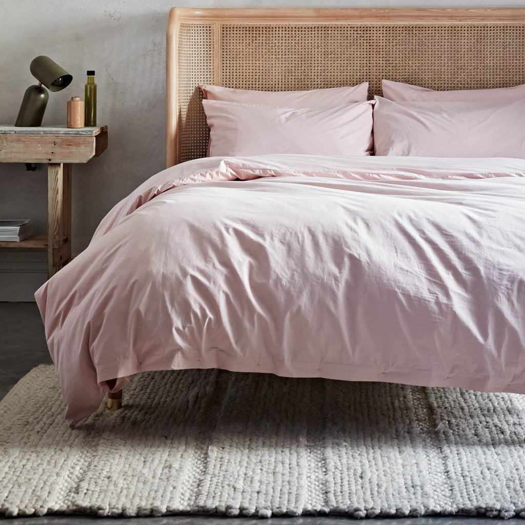Bed with pink bedding and wicker headboard in a bedroom setting
