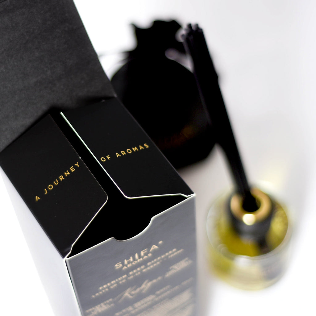 Black and white packaging of 'A Journey of Aromas' with a blurred bottle in the background.
