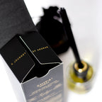 Black and white packaging of 'A Journey of Aromas' with a blurred bottle in the background.
