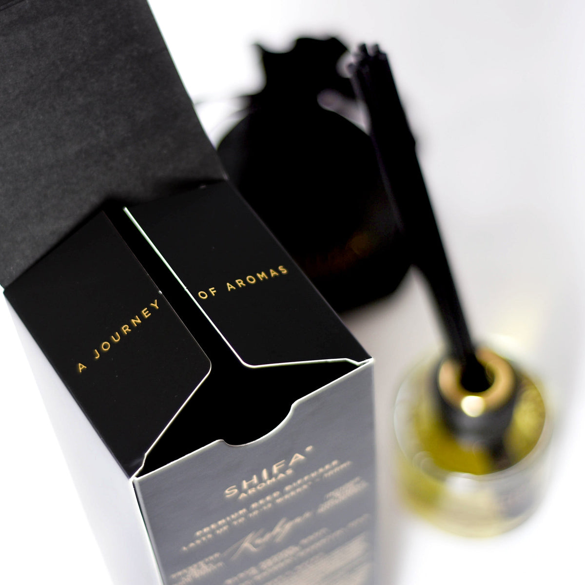 Black and white packaging of 'A Journey of Aromas' with a blurred bottle in the background.