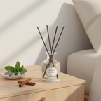Diffuser with reeds on a wooden surface next to a plate with leaves and cinnamon sticks, against a neutral background.