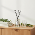 Reed diffuser with black sticks on a wooden surface with books and a glass.