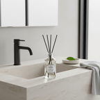 Bottle of diffuser on a bathroom counter with a black faucet and white sink.