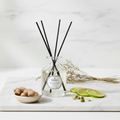 Diffuser bottle with black sticks on a marble surface with ginger and limes.