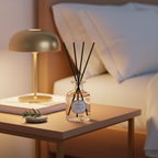 Diffuser with reeds on a bedside table next to a lamp and books, with a cozy bedroom setting.