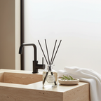 Diffuser with black sticks on a bathroom counter with a sink and towel in the background