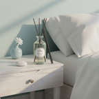 Diffuser with sticks on a nightstand next to a bed
