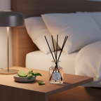 Diffuser with black sticks on a wooden table next to a bed with white pillows.