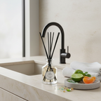 Diffuser with black sticks on a bathroom counter with a sink and towel in the background