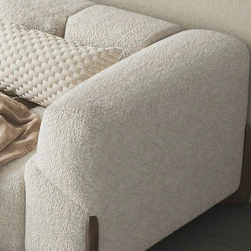 Close-up of a textured beige sofa with a pillow and blanket.