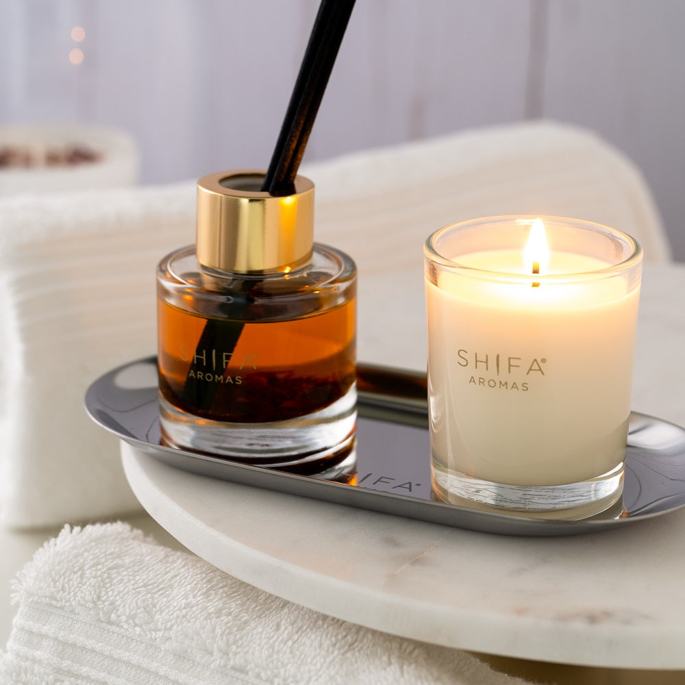 Shifa Aromas diffuser and candle on a marble tray with white towels in the background