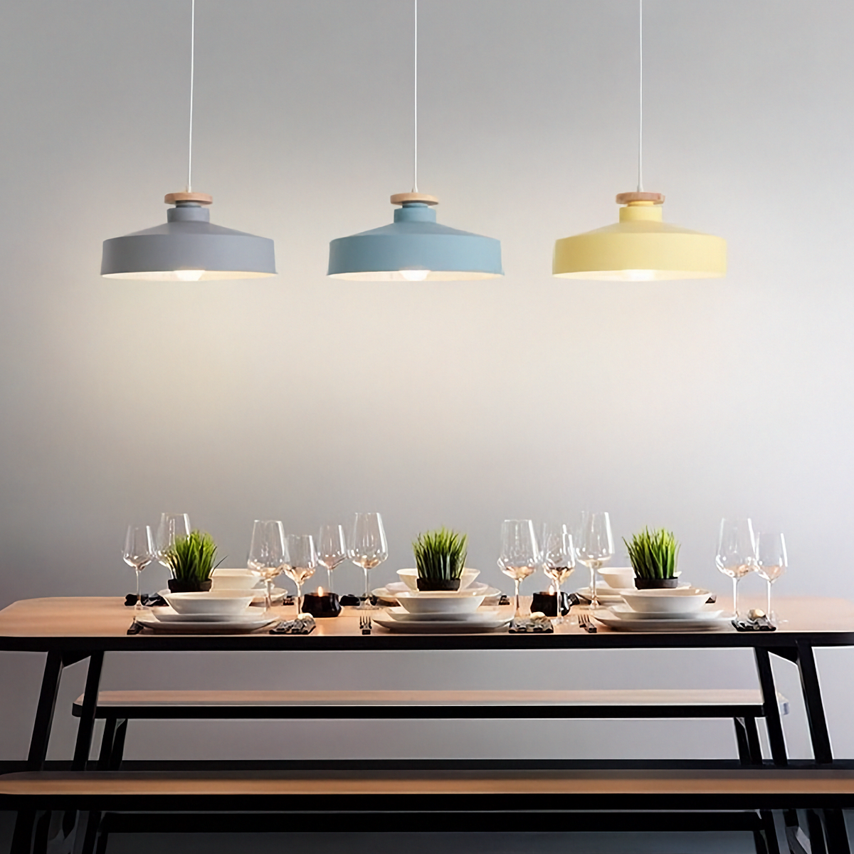 Dining table set with wine glasses and plates under three pendant lights in a modern kitchen.