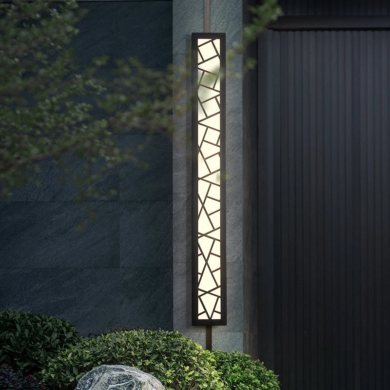 Decorative outdoor wall light fixture on a dark wall with greenery.