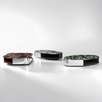 Three modern oval side tables with polished chrome bases and marble tops in brown, black, and green, arranged on a reflective white surface against a light gray background.