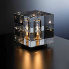 Modern glass cube table lamp with multiple light bulbs on a dark surface.