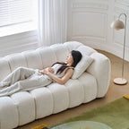 Woman lying on a large, plush white sofa in a bright room with a lamp and rug.
