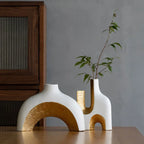 Two unique ceramic vases with gold accents on a wooden surface against a gray wall.