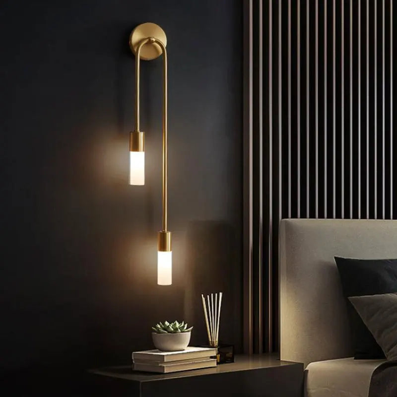 Modern wall sconce with two lights on a dark wall next to a bed.