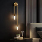 Modern wall sconce with two lights on a dark wall next to a bed.