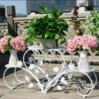 Decorative white metal plant stand with flowers and plants on a wooden deck.