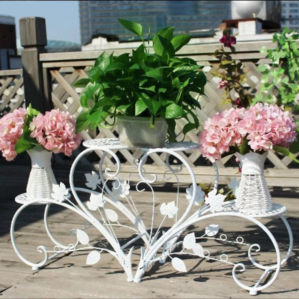 Decorative white metal plant stand with flowers and plants on a wooden deck.