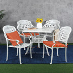 Outdoor patio set with white chairs, orange cushions, and a glass table against a gray wall.