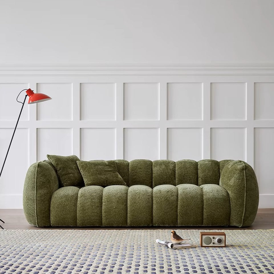 Green sofa in a room with a white paneled wall and a red lamp.
