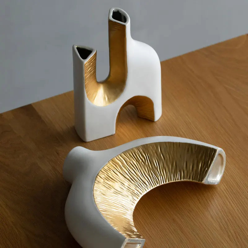 Two modern ceramic vases with gold interior on a wooden surface.
