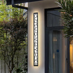 Modern outdoor wall light fixture on a building exterior with greenery around.