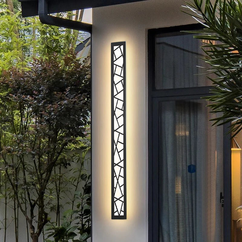 Modern outdoor wall light fixture on a building exterior with greenery around.