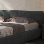 Gray upholstered bed with brown pillows and blanket in a bedroom setting