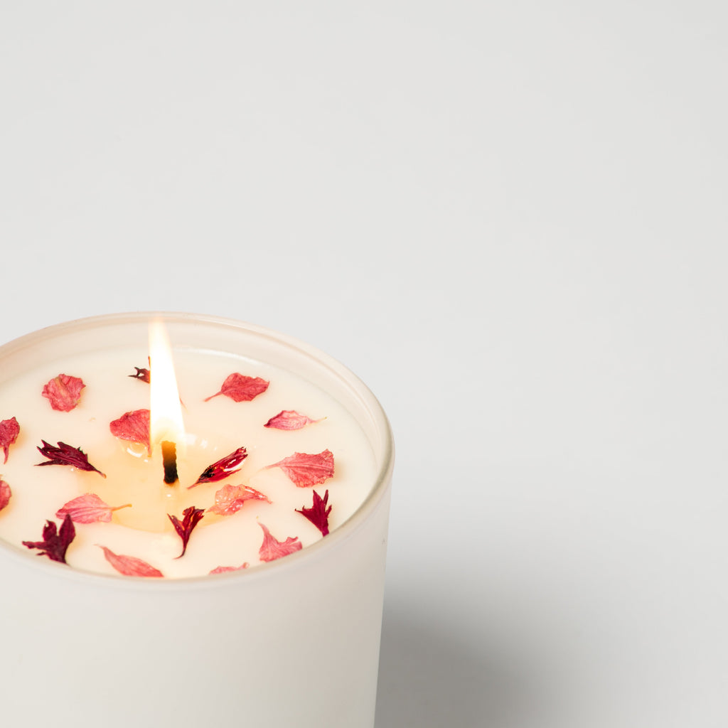 Candle with floral petals burning on a light gray background