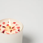Candle with floral petals burning on a light gray background