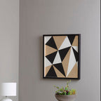 Geometric abstract art piece on a gray wall with a lamp and plant in the foreground.