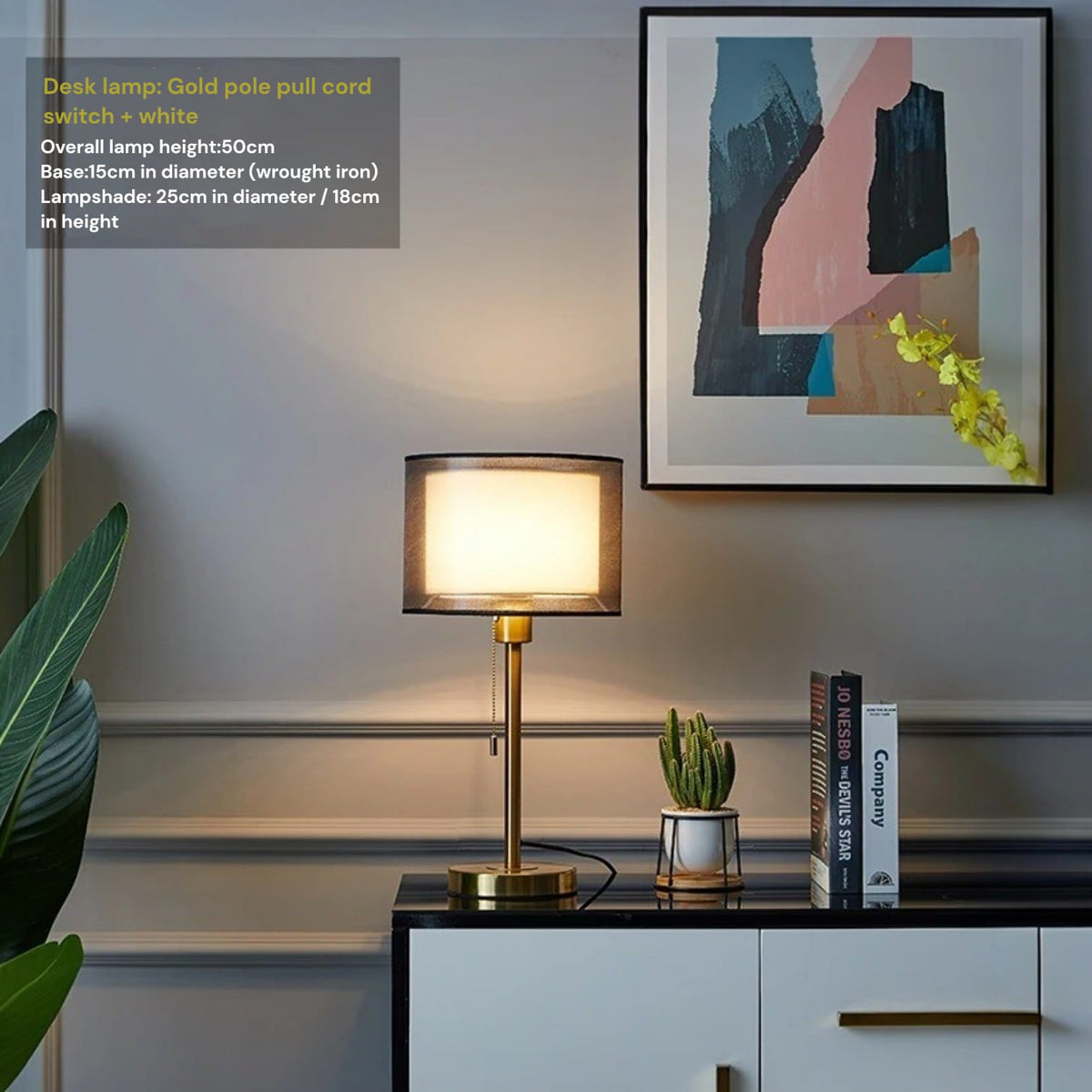 Modern desk lamp on a surface with books and a plant, framed abstract art on the wall.