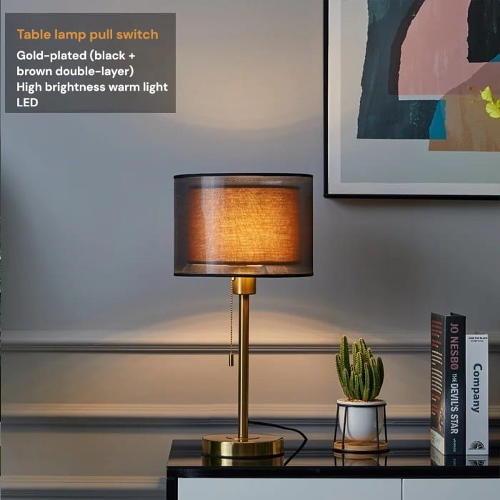 Table lamp with gold-plated pull switch on a desk with books and a plant.
