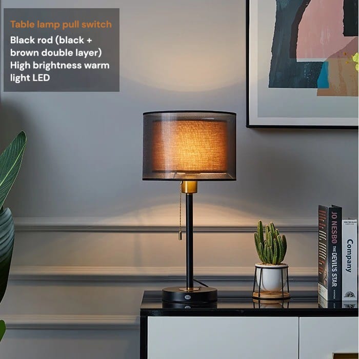 Table lamp with black rod and double-layered design on a shelf with books and a plant.