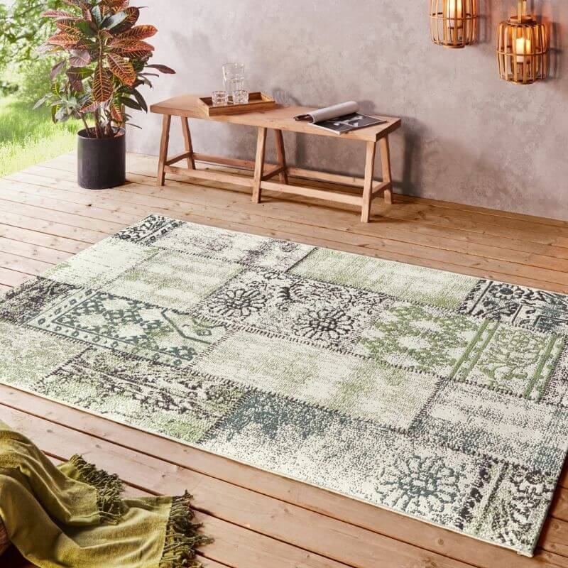 Patterned rug on a wooden deck with a wooden table and plants in the background.