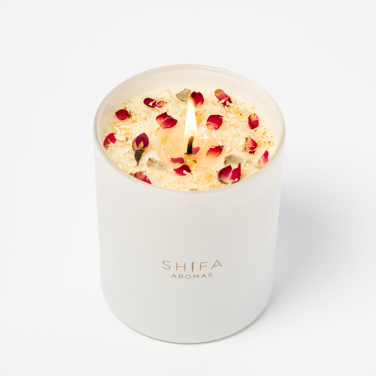 Candle with floral petals in a white container labeled 'Shifa Aromas' on a light background