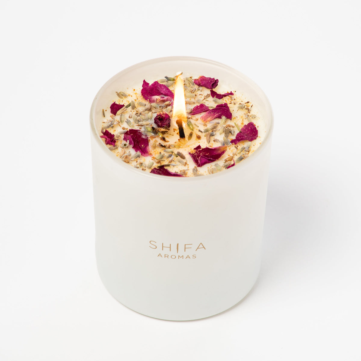 White candle with rose petals in a white container labeled 'SHIFA AROMAS' on a white background