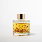 Glass jar with gold cap containing a yellow liquid on a white background