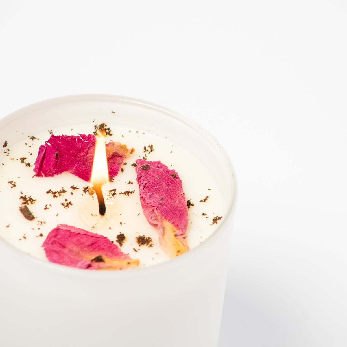 Candle with pink floral petals and a flame on a white background