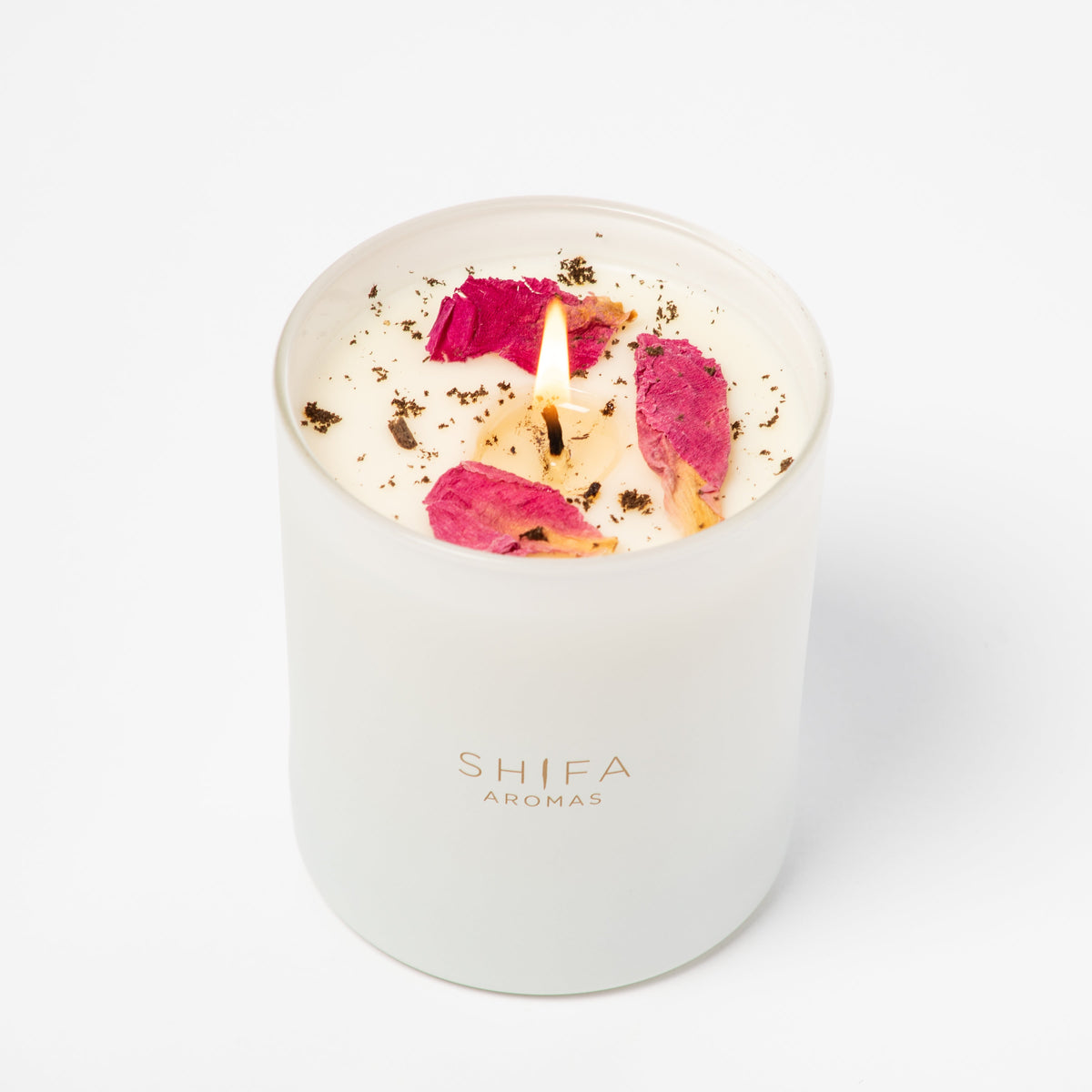 Candle with pink petals in a white container labeled 'Shifa Aromas' on a white background