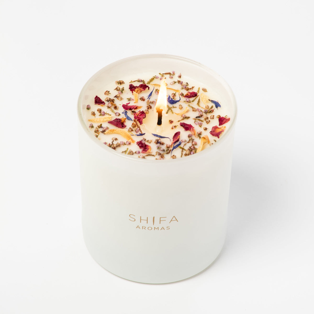 White candle with colorful dried flowers on a white background, branded 'Shifa Aromas'.