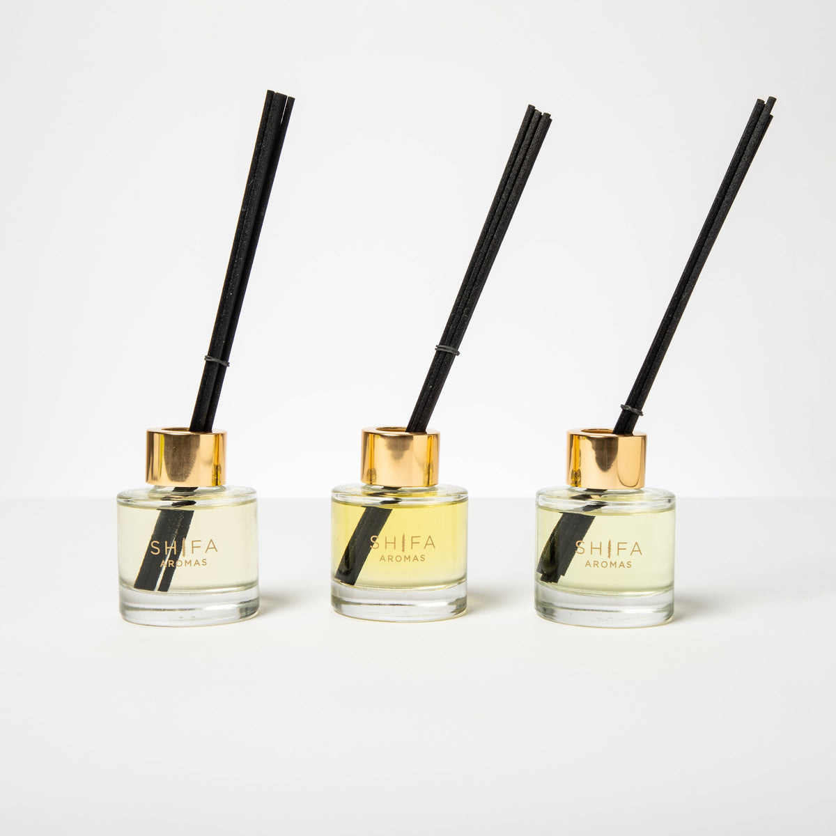 Three Shifa Aromas diffusers with black sticks on a white background