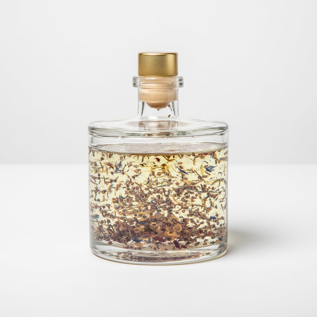 Glass jar with gold cap containing a mixture of herbs on a white background