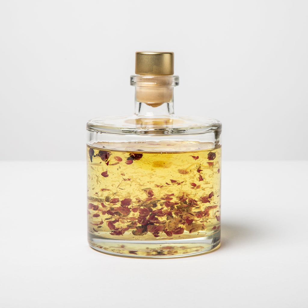 Glass bottle with gold cap containing a yellow liquid with red and brown bits on a white background