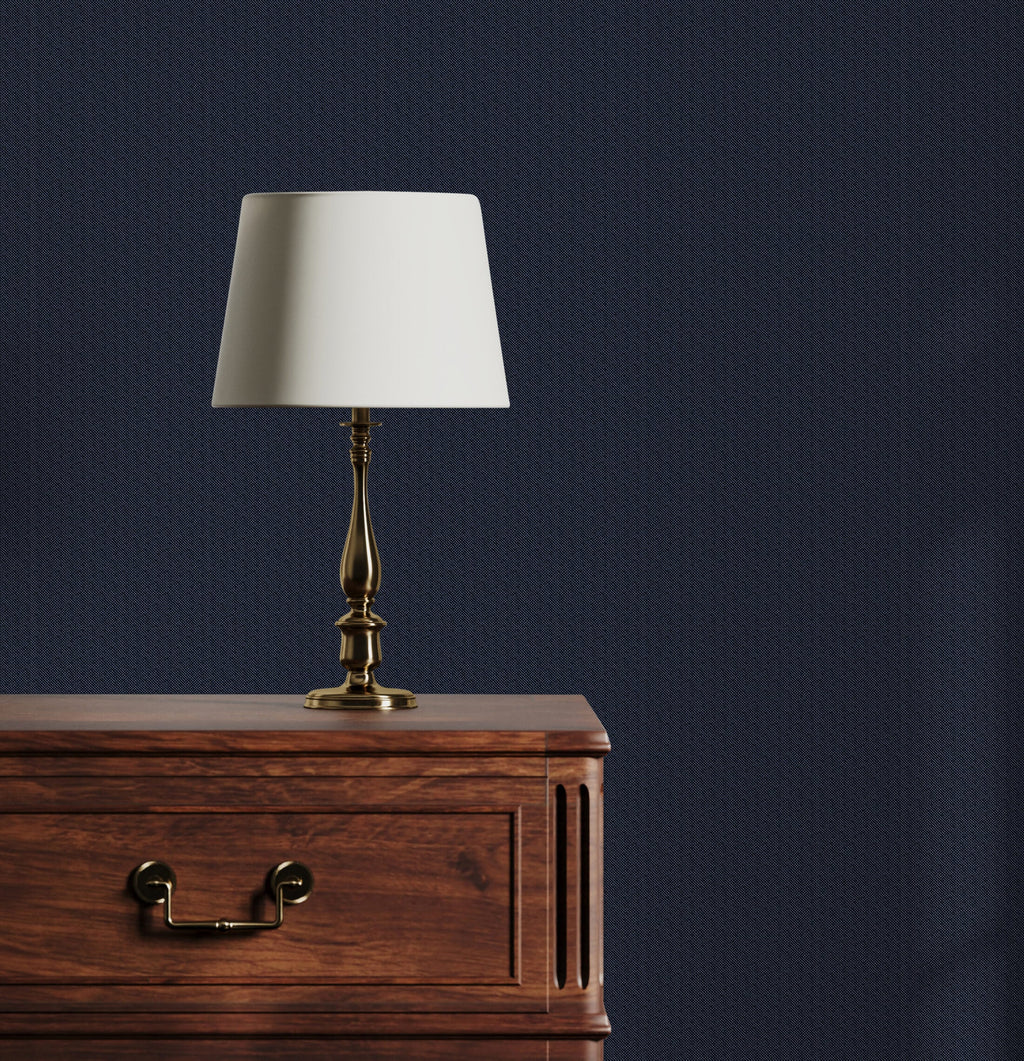 Table lamp with white shade on a wooden table against a dark blue wall
