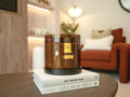 Brown candle with a gold label on top of books in a living room setting