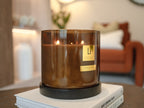 Brown candle with a label on top of books in a blurred indoor setting